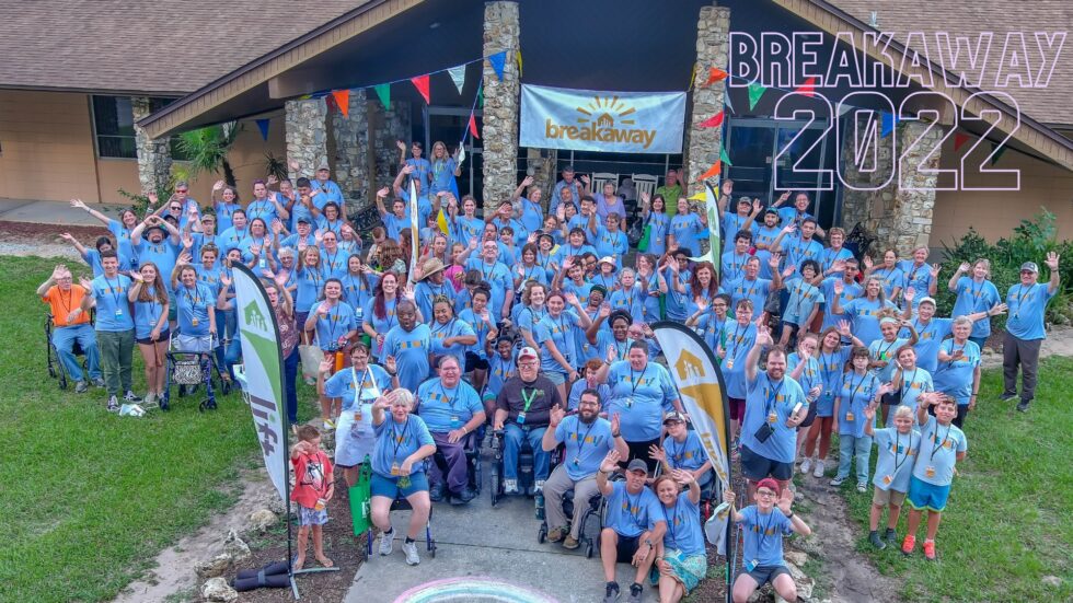 Campers and Volunteers at Breakaway Camp in 2022.  They are standing on green grass in front of a building and most of them are wearing blue camp tshirts.