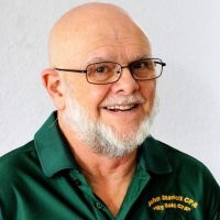 John Stancil: Man with trimmed white beard, shaven head, glasses, and a green polo shirt