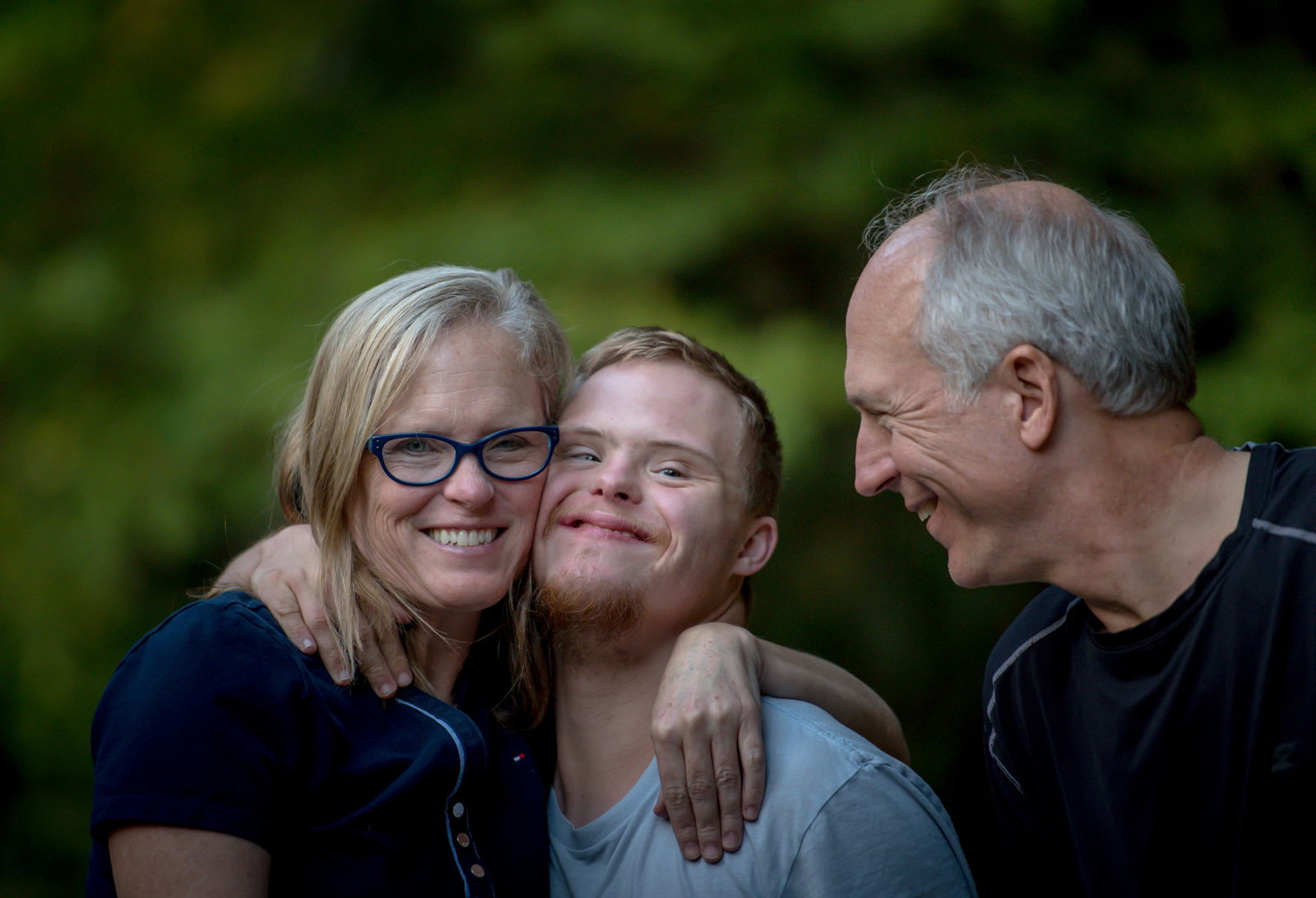 Young man with disability hugging his mom.  Dad looks on smiling.