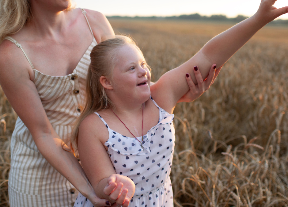 Mother and daughter wearing dresses standing in a field.  Mother is holding daugher's arms.